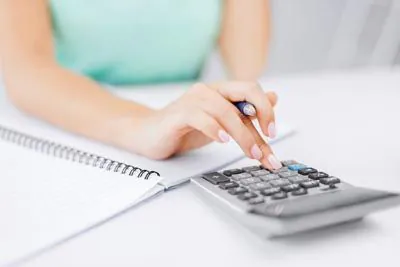 Hand using calculator beside spiral notebook